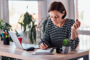 Lady writing in her notebook (infront of a laptop)