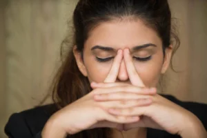 Woman holding her nose while closing her eyes and thinking deeply