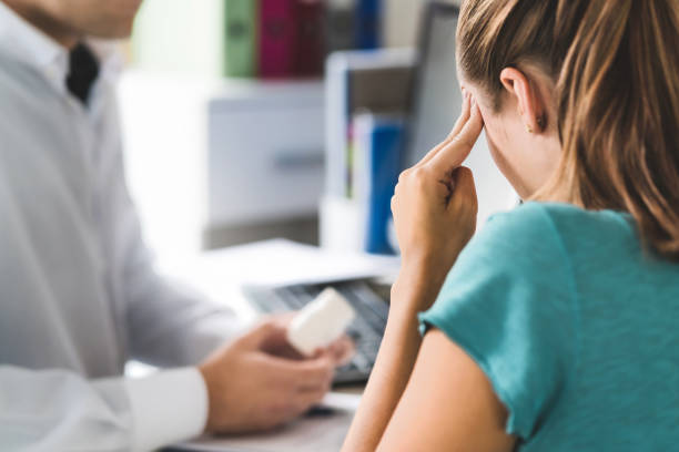 Woman holding her temple while talking to a doctor